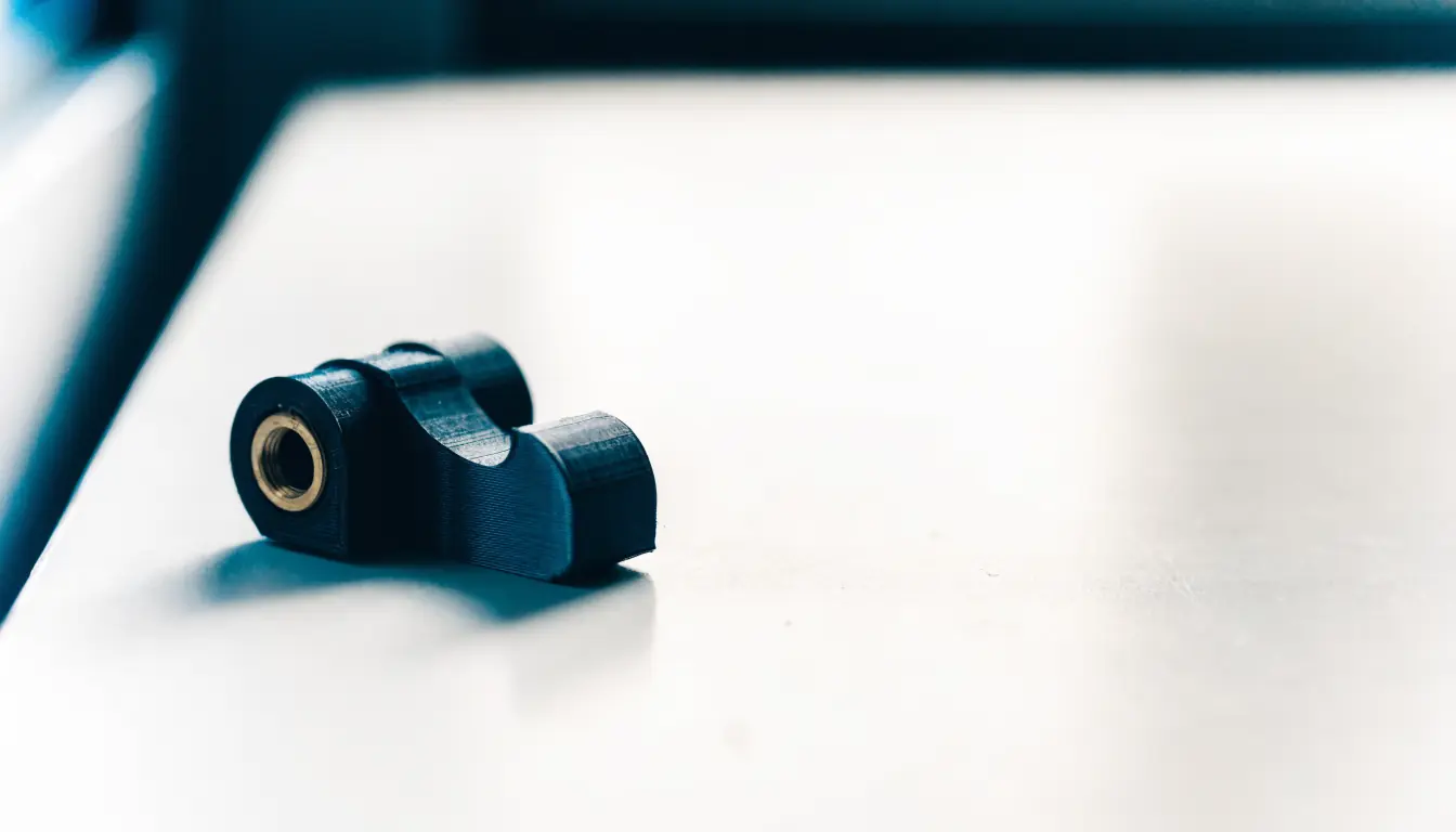 3D-gedrucktes Funktionsbauteil aus dunklem Polymer mit eingesetzter Messing-Gewindebuchse