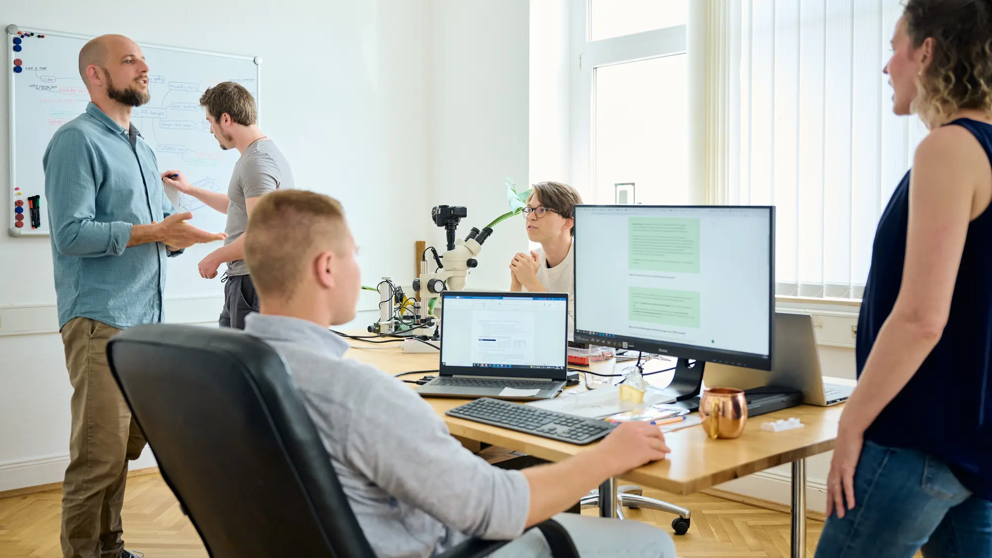 Das Team von Hoelzel Engineering im Entwicklungsbüro in Sankt Augustin: Besprechung am Whiteboard, Arbeitsplätze mit Mikroskop und CAD